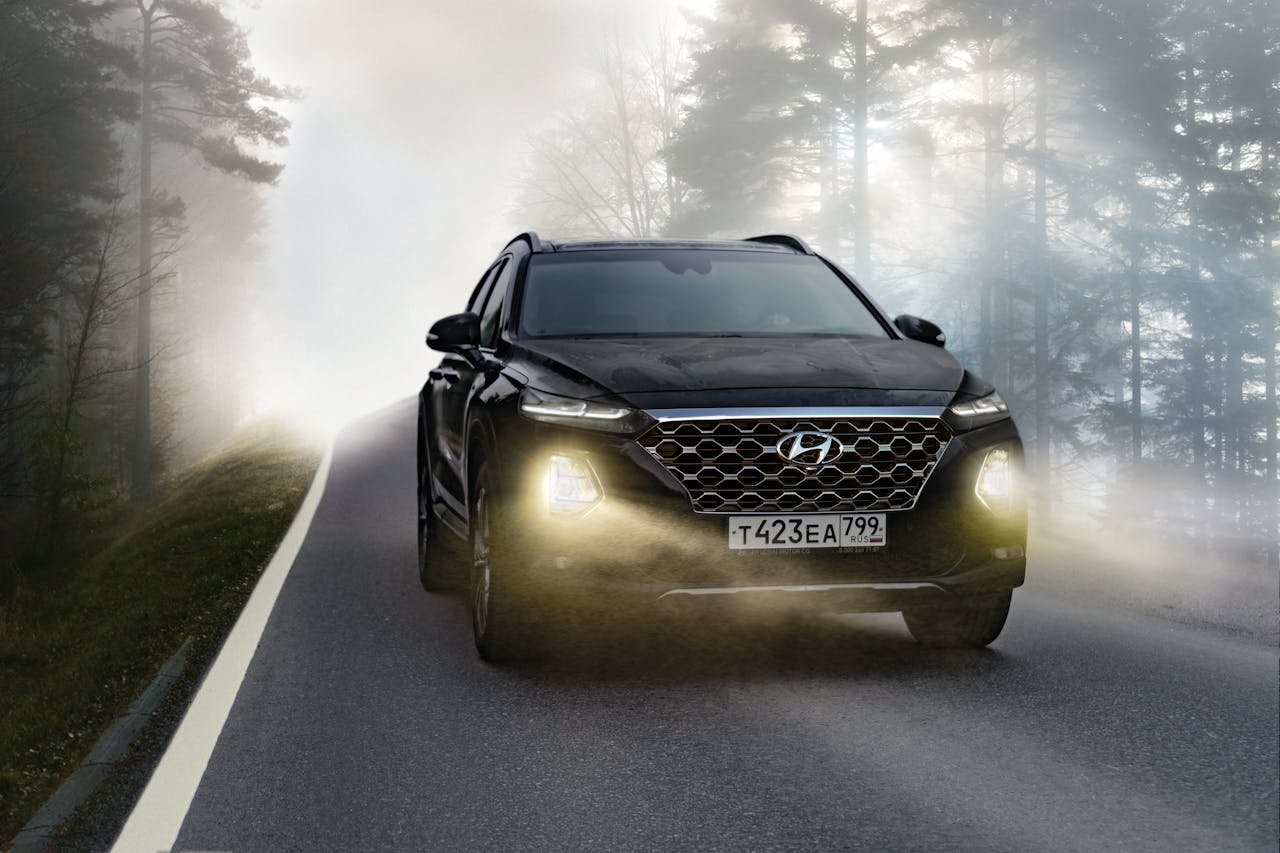 Black SUV driving on a misty forest road with headlights on, creating a dramatic scene.